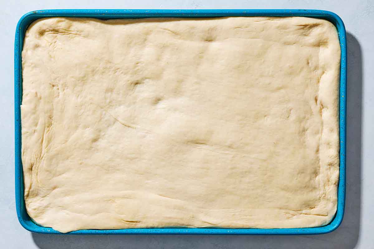 An overhead photo of unbaked sfincione sicilian pizza dough spread on a baking sheet.