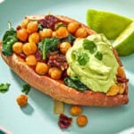 A close up of a stuffed sweet potato with a dollop of avocado crema on a plate with 2 lime wedges.