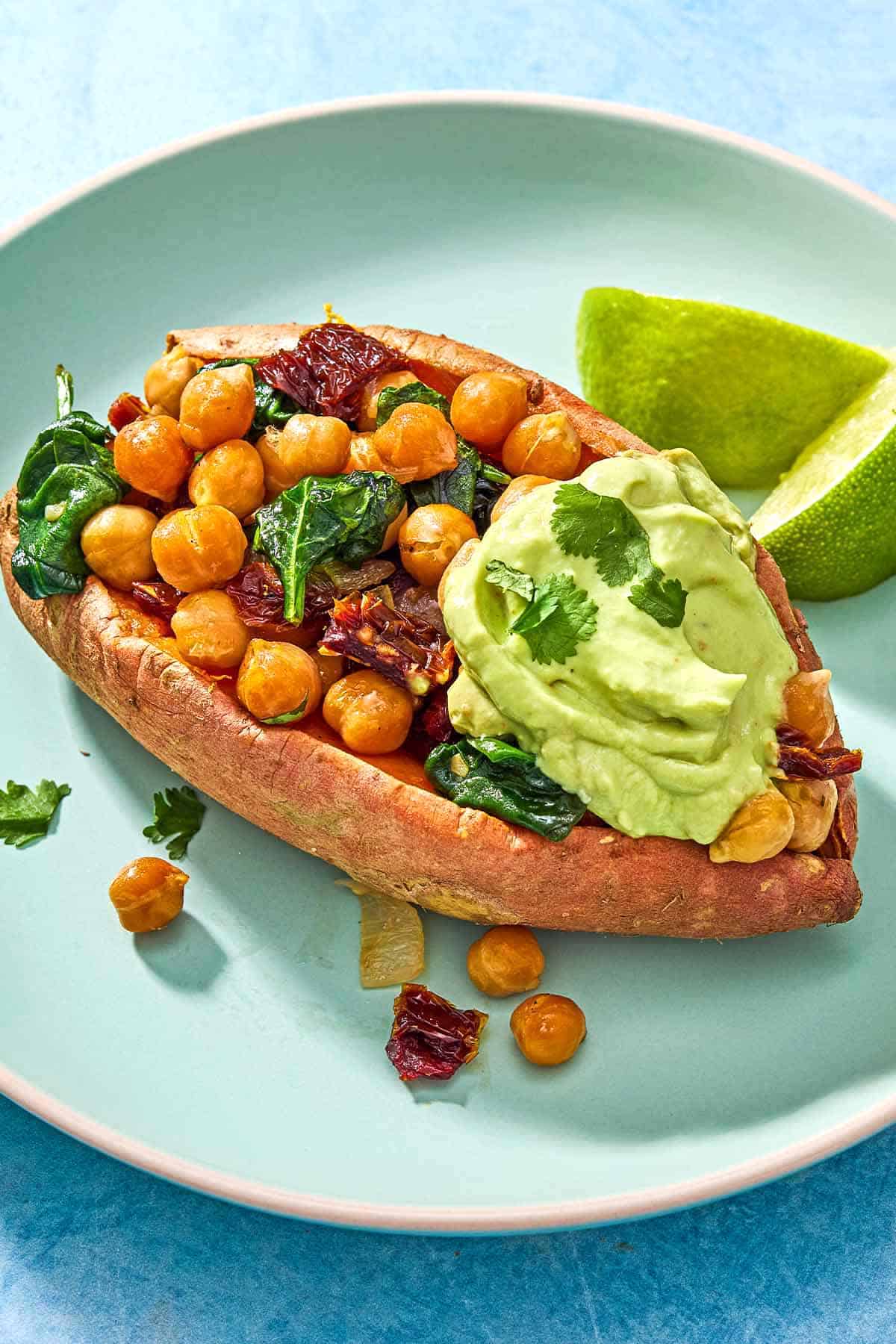 A close up of a stuffed sweet potato with a dollop of avocado crema on a plate with 2 lime wedges.