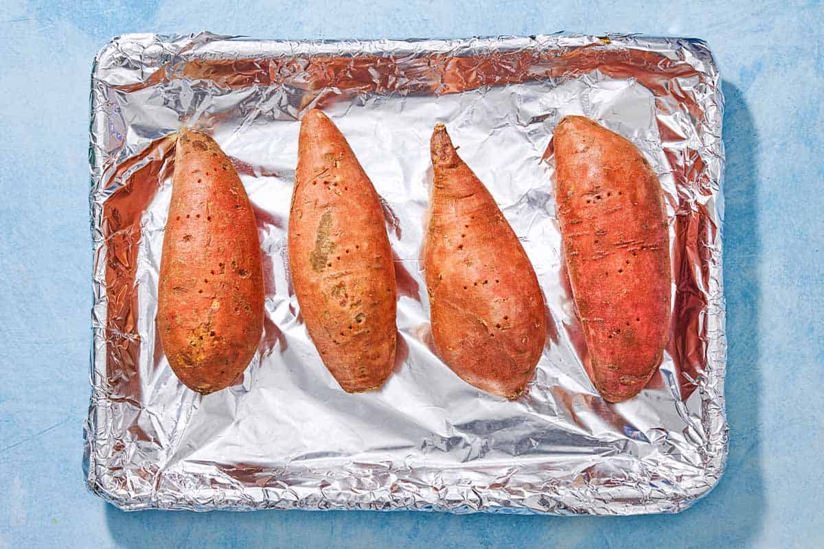 An overhead photo of 4 sweet potatoes on a foil-lined sheet pan.