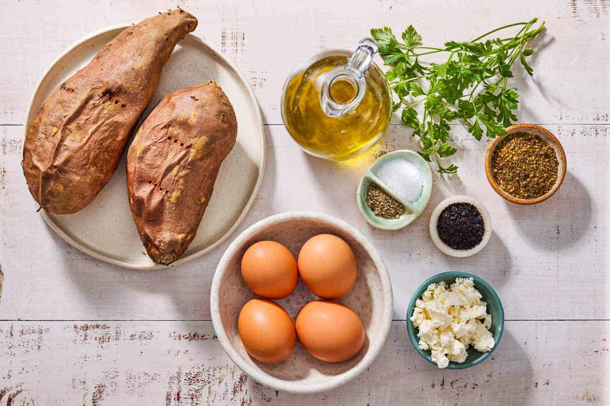 Ingredients for sweet potato breakfast with fried eggs including sweet potatoes, eggs, olive oil, salt, black pepper, feta, za'atar, urfa biber and parsley.