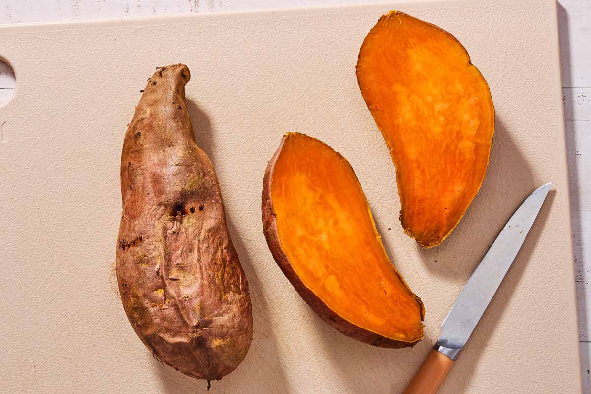 2 cooked sweet potatoes on a cutting board with a knife. One is cut in half.