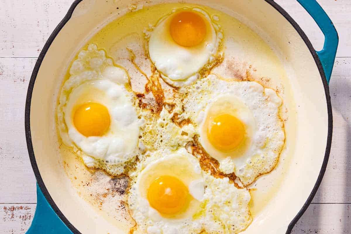 An overhead photo of 4 eggs being fried in a skillet.