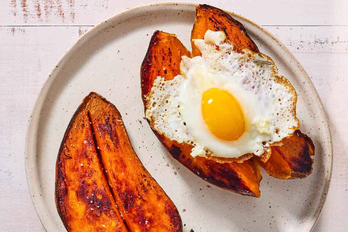 An overhead photo of 2 baked sweet potatoes on a plate. One is topped with a fried egg.