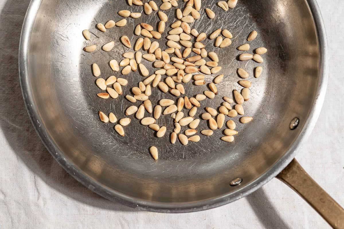 An overhead photo of pine nuts being toasted in a skillet.