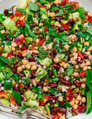 An overhead photo of a Mediterranean three bean salad in a serving bowl with two forks. Next to this is a kitchen towel.