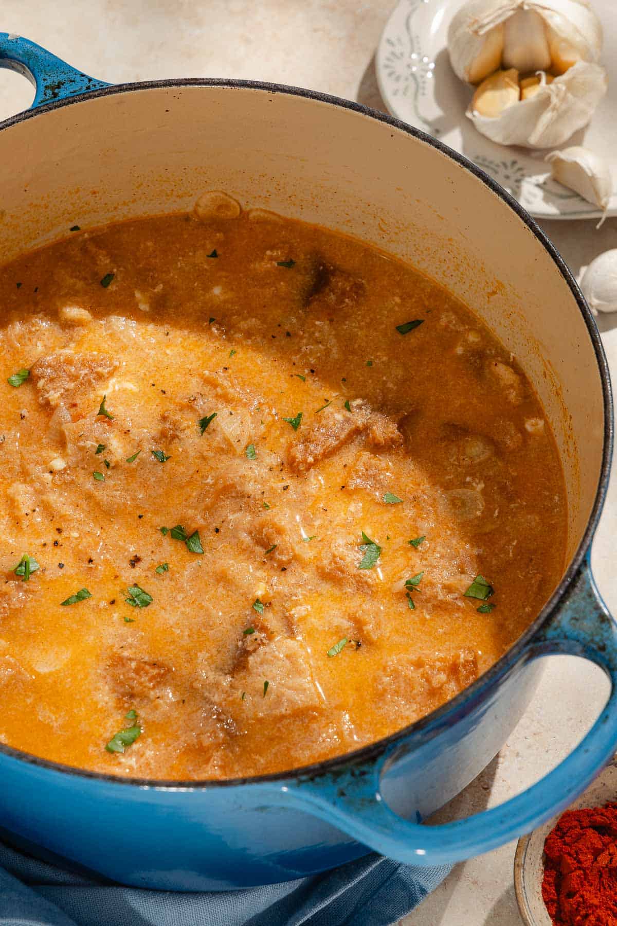 Sopa de ajo in a large pot. Next to this is a cloth napkin, a bowl of smoked paprika and garlic cloves on a small plate.