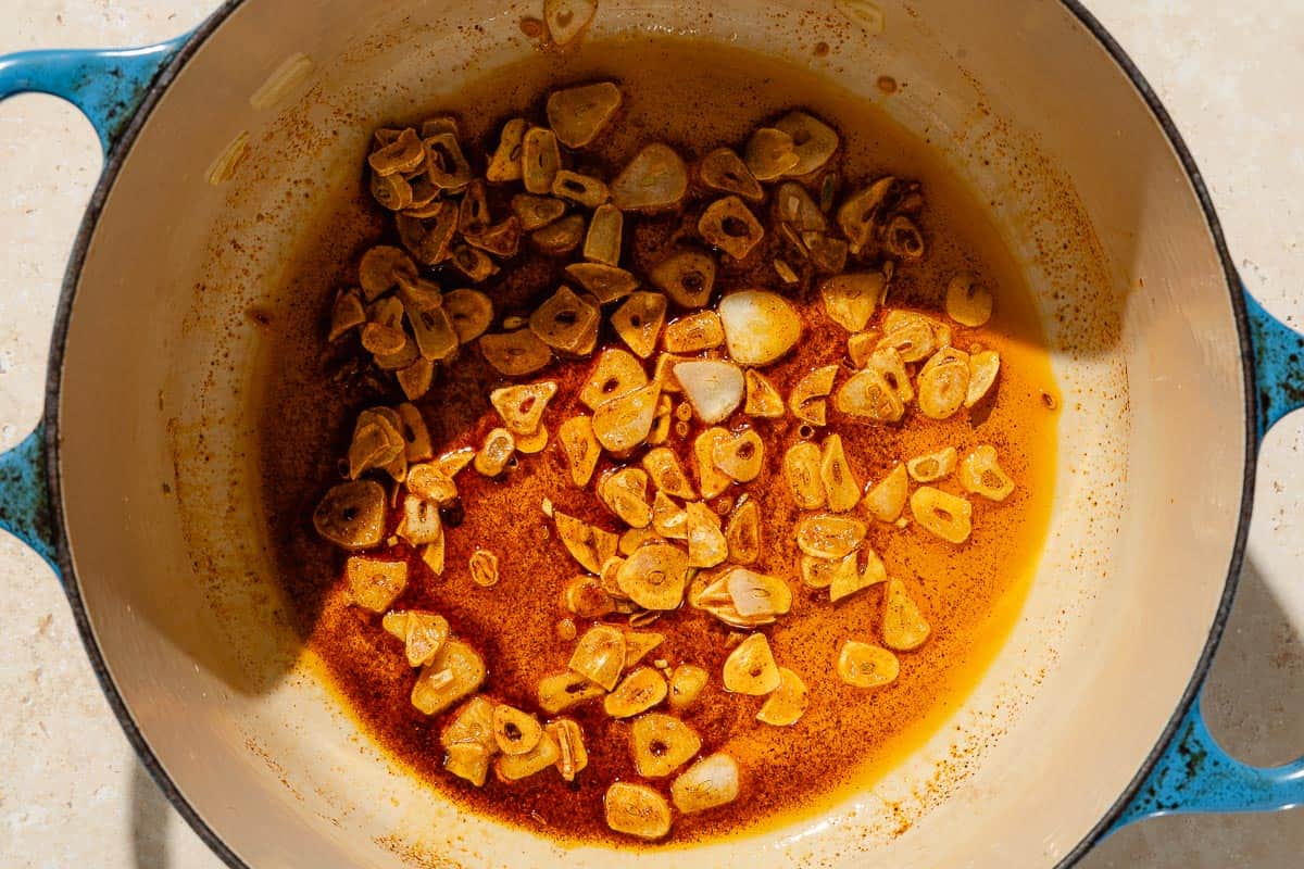 An overhead photo of sliced garlic after being sauteed in olive oil in a large pot.