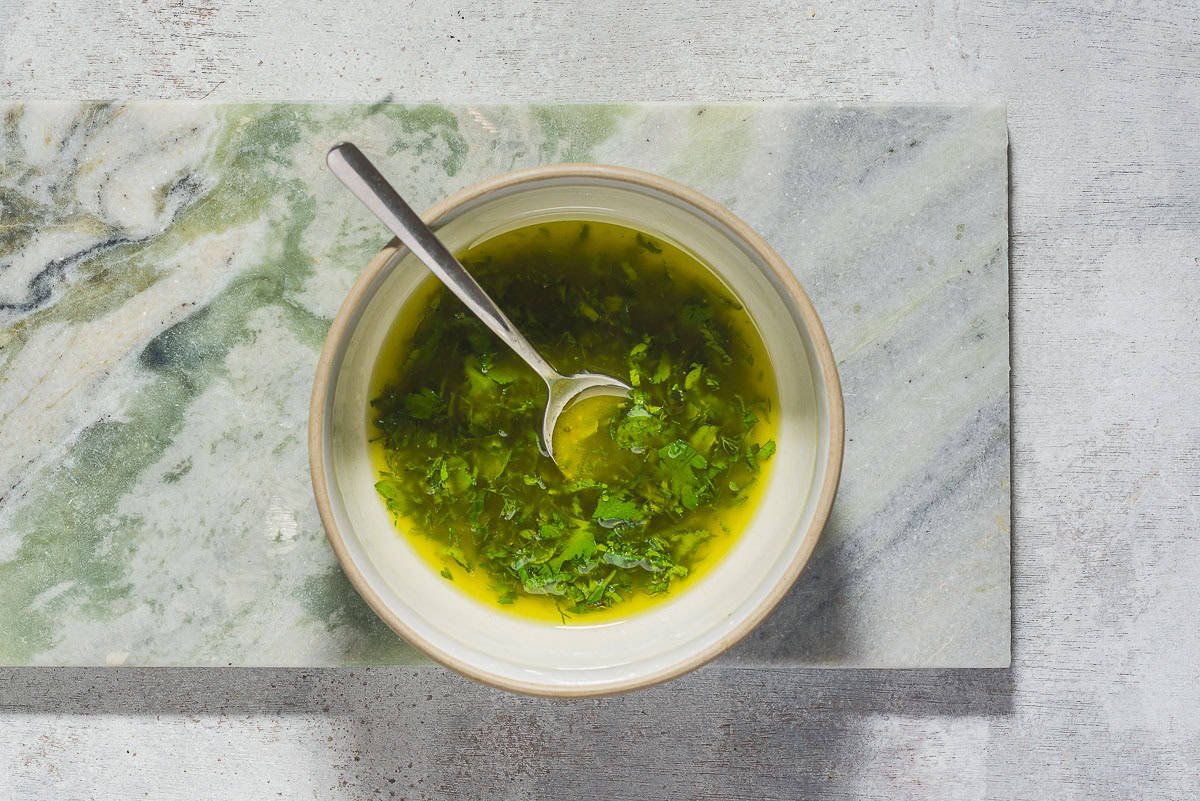 An overhead photo of the lemon herb dressing for the poached chicken breasts in a bowl with a spoon.