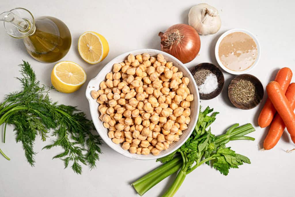 Ingredients for revithosoupa Greek chickpea soup including chickpeas, dill, celery, carrots, lemon, olive oil, garlic, onion, salt, black pepper, oregano and tahini.