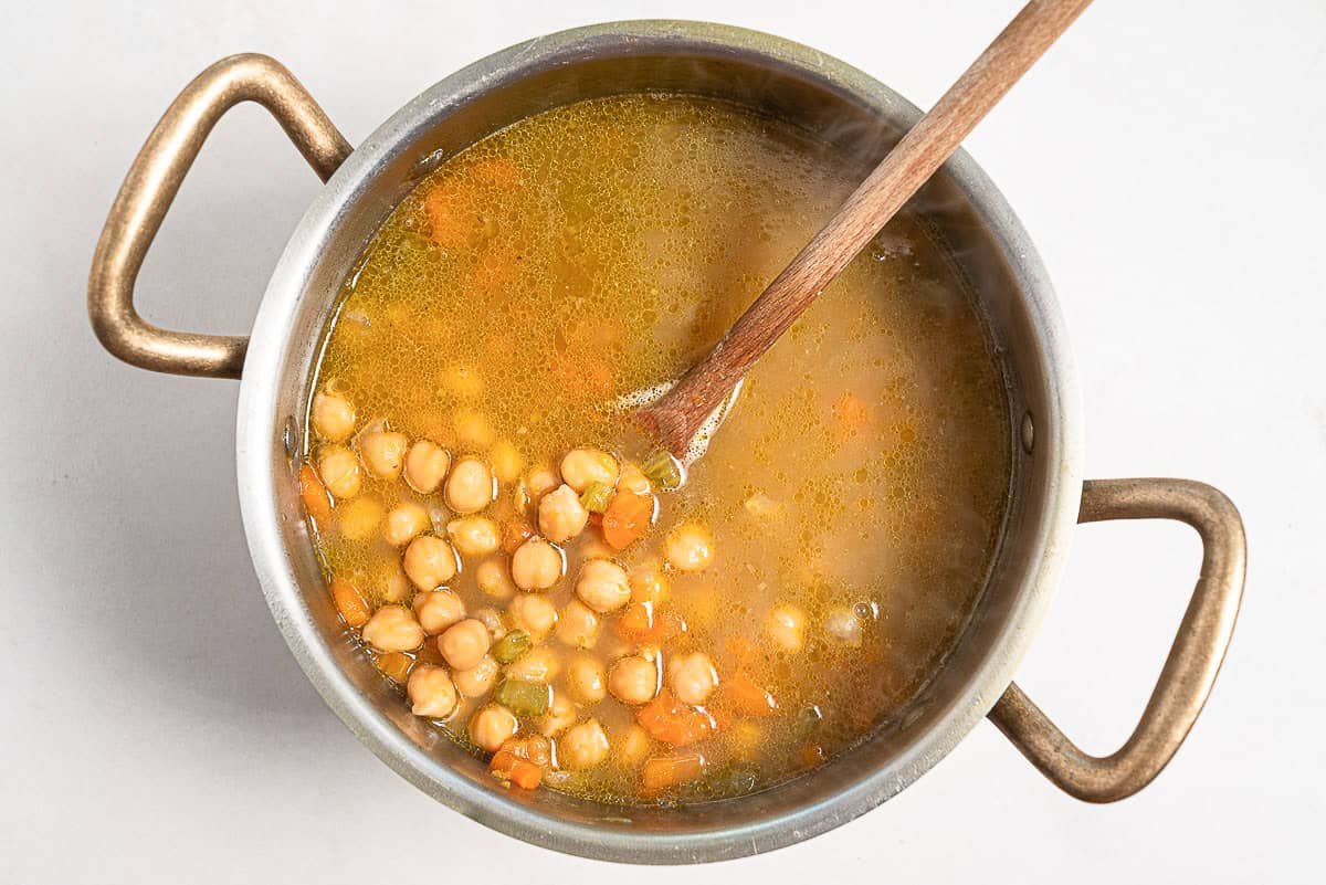 The revithosoupa Greek chickpea soup simmering in a large pot with a wooden spoon.