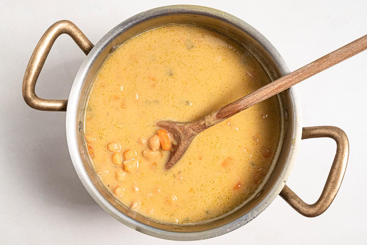 An overhead photo of the revithosoupa Greek chickpea soup just after the tahini was added in a large pot with a wooden spoon