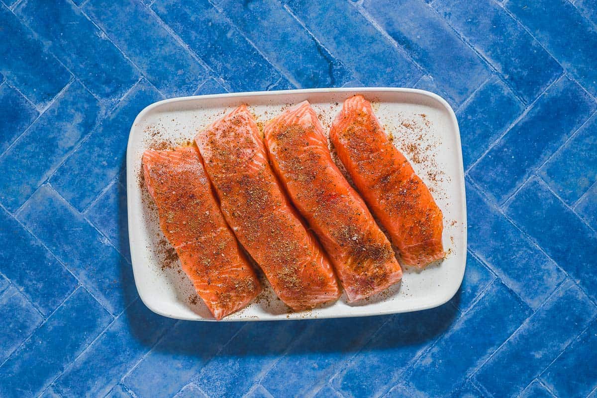 An overhead photo of 4 uncooked seasoned salmon fillets on a platter.