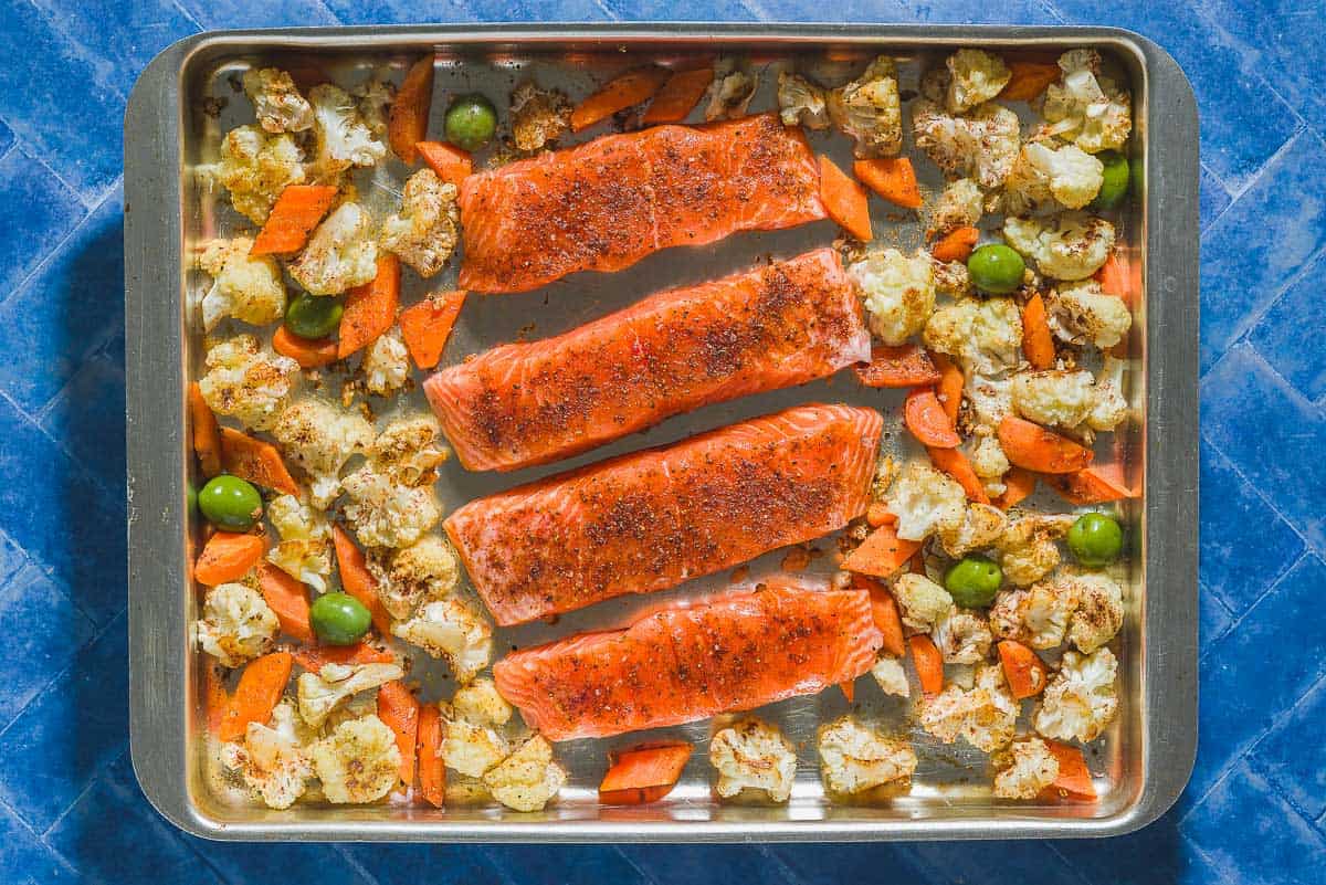 An overhead photo of uncooked salmon fillets with the roasted vegetables on a sheet pan.