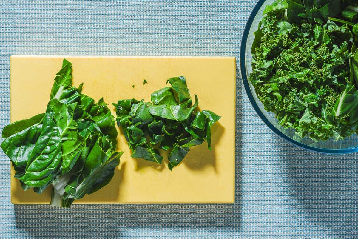 An overhead photo of some greens on a cutting board. Half have been chopped. Next to this is a bowl of the cooking greens.