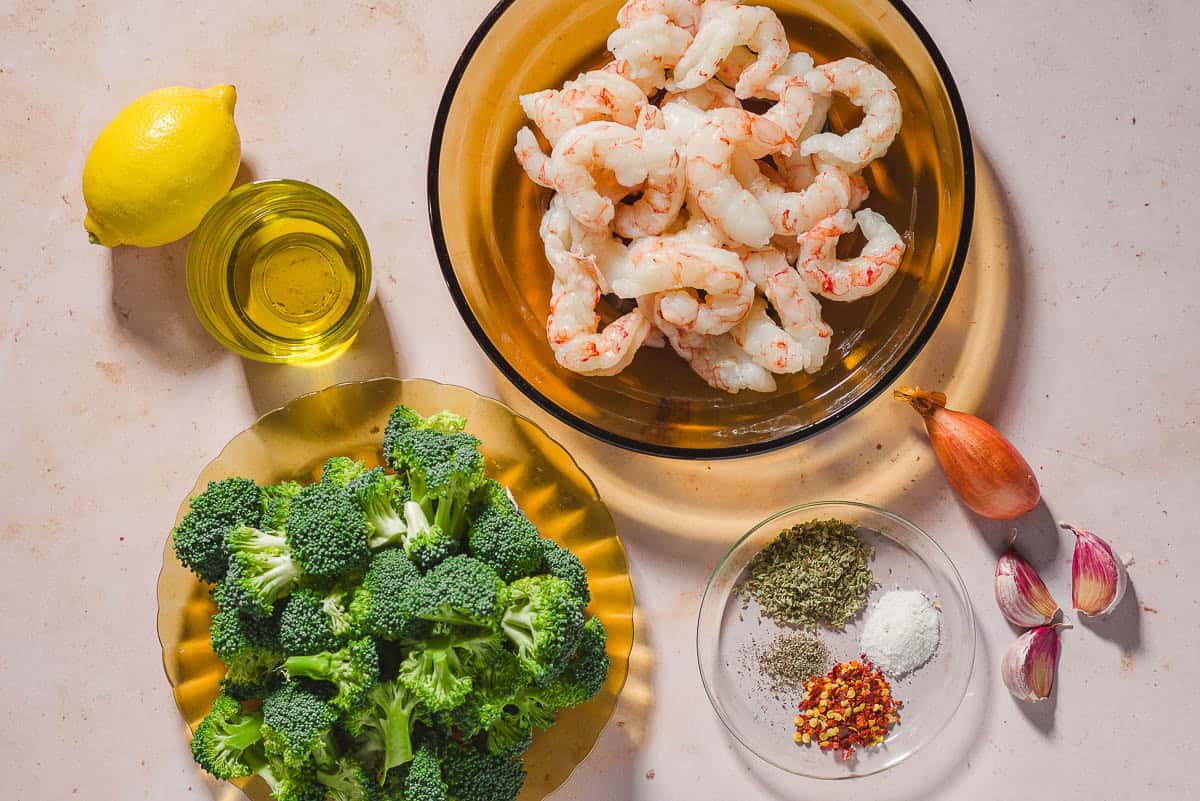 Ingredients for the shrimp and broccoli recipe including shrimp, broccoli, a shallot, garlic, lemon , olive oil, salt, black pepper, oregano, and red pepper flakes.