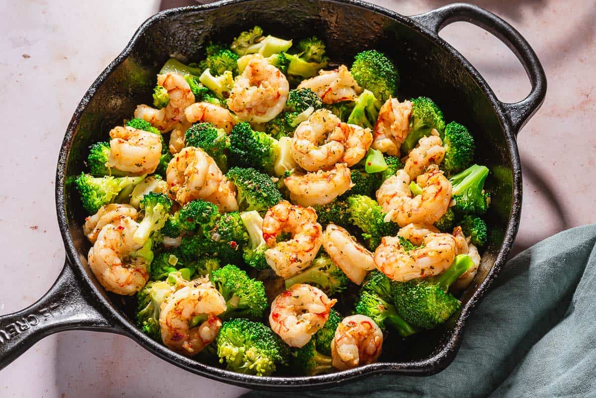 A close up of the cooked shrimp and broccoli skillet. Next to this is a cloth napkin.