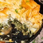 A close up of vegan skillet spanakopita in a skillet with one slice removed.