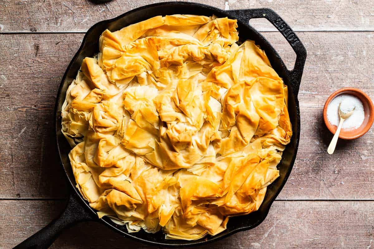 An overhead photo of vegan skillet spanakopita in a skillet next to a bowl of salt.