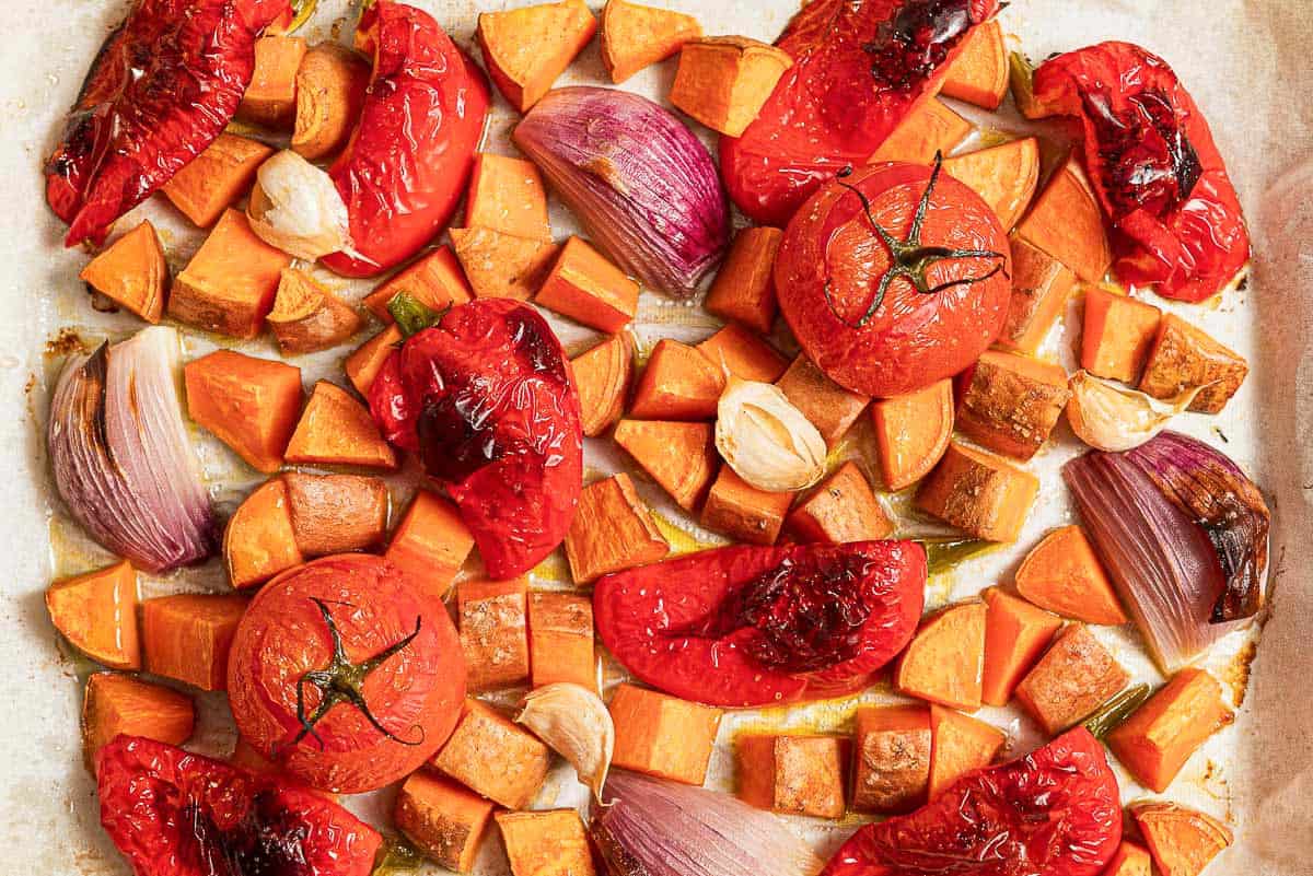 An overhead photo of the roasted vegetables for the sweet potato soup recipe on a parchment lined sheet pan.