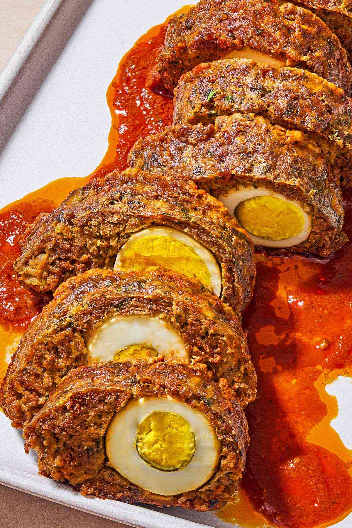 A close up of sliced greek meatloaf with hardboiled eggs and sauce on a platter.