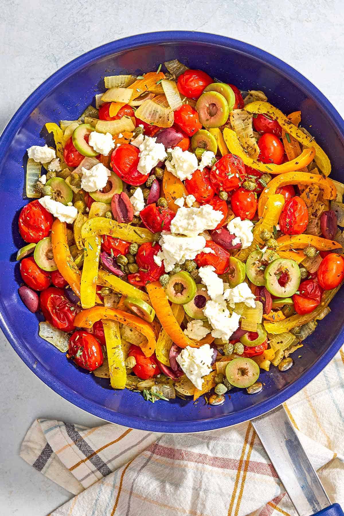 An overhead photo of Mediterranean vegetable medley in a skillet. Next to this is a kitchen towel.