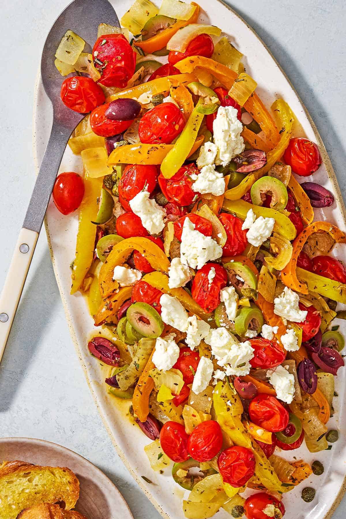 An overhead photo of Mediterranean vegetable medley on a platter with a serving spoon.