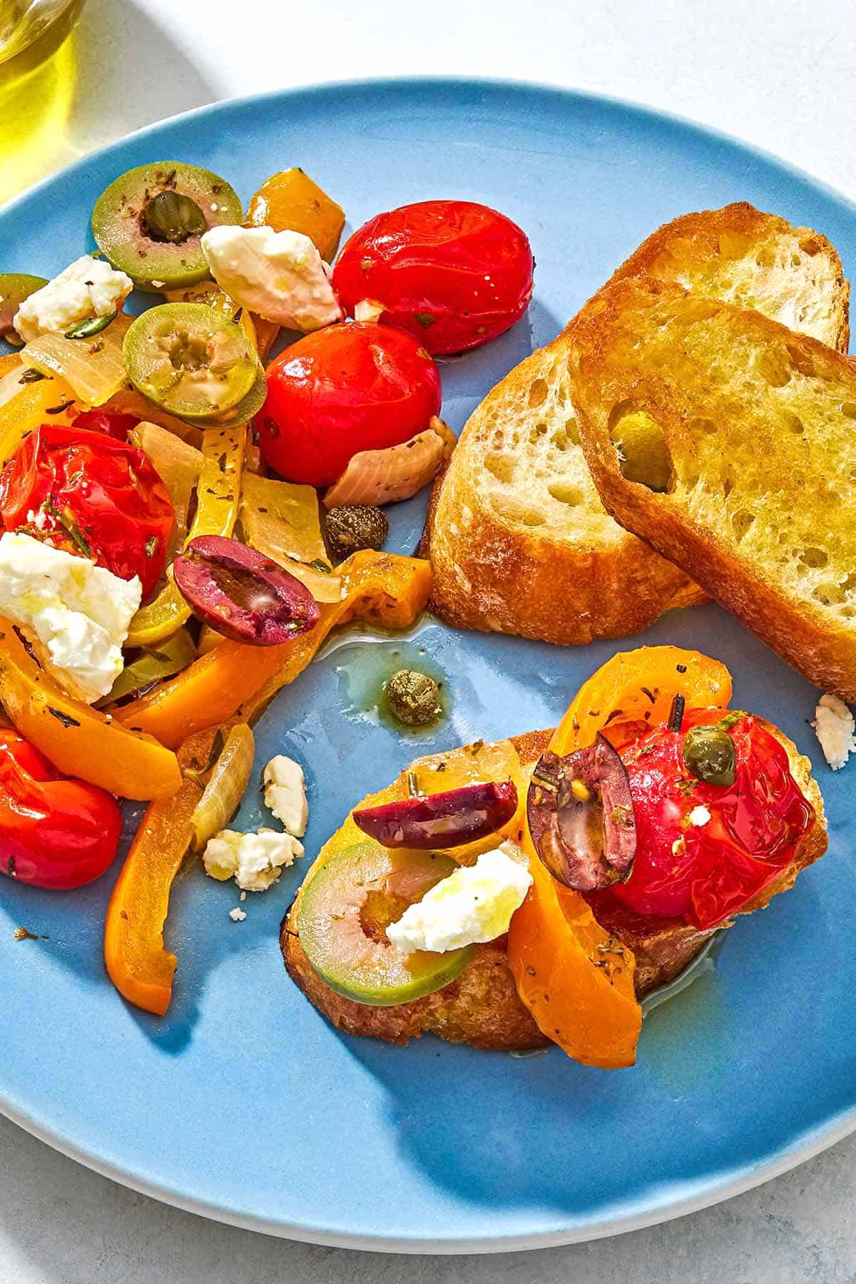 A close up of a serving of Mediterranean vegetable medley on a plate with 2 slices of a toasted baguette.