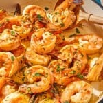 A close up of shrimp scampi in a skillet with a wooden spoon.