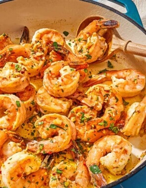 A close up of shrimp scampi in a skillet with a wooden spoon.