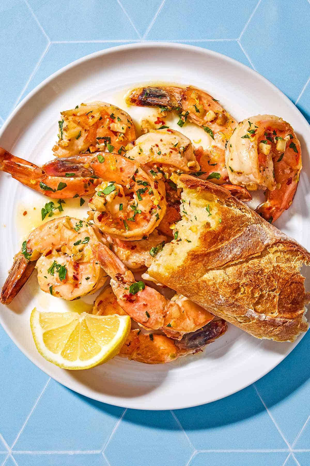 An overhead photo of shrimp scampi on a plate with a lemon slice and a piece of crusty bread.