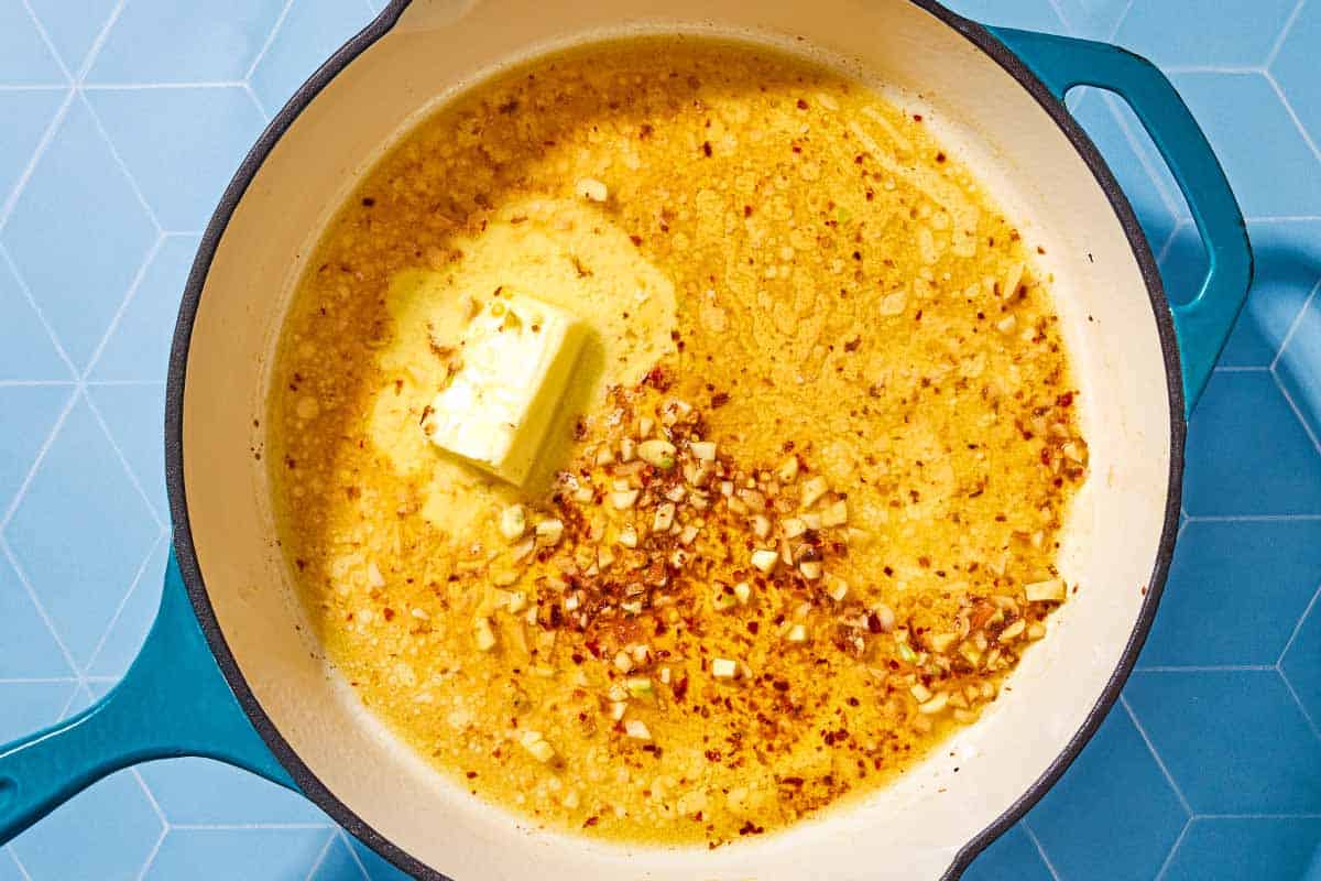 An overhead photo of the butter for the shrimp scampi recipe being melted in a skillet with olive oil, garlic, red pepper flakes, white wine and lemon juice.