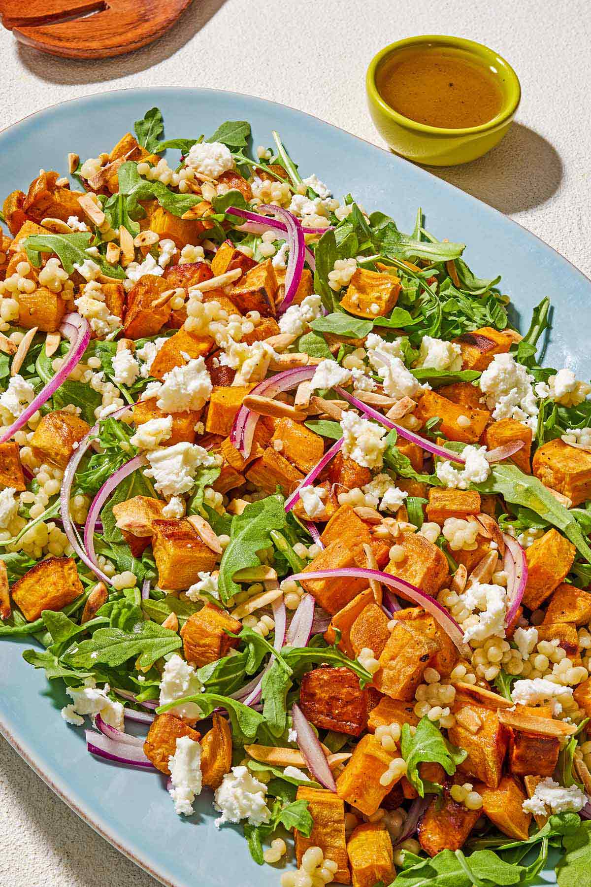 The sweet potato salad on a platter next to a set of wooden serving utensils and a small bowl of the dressing.