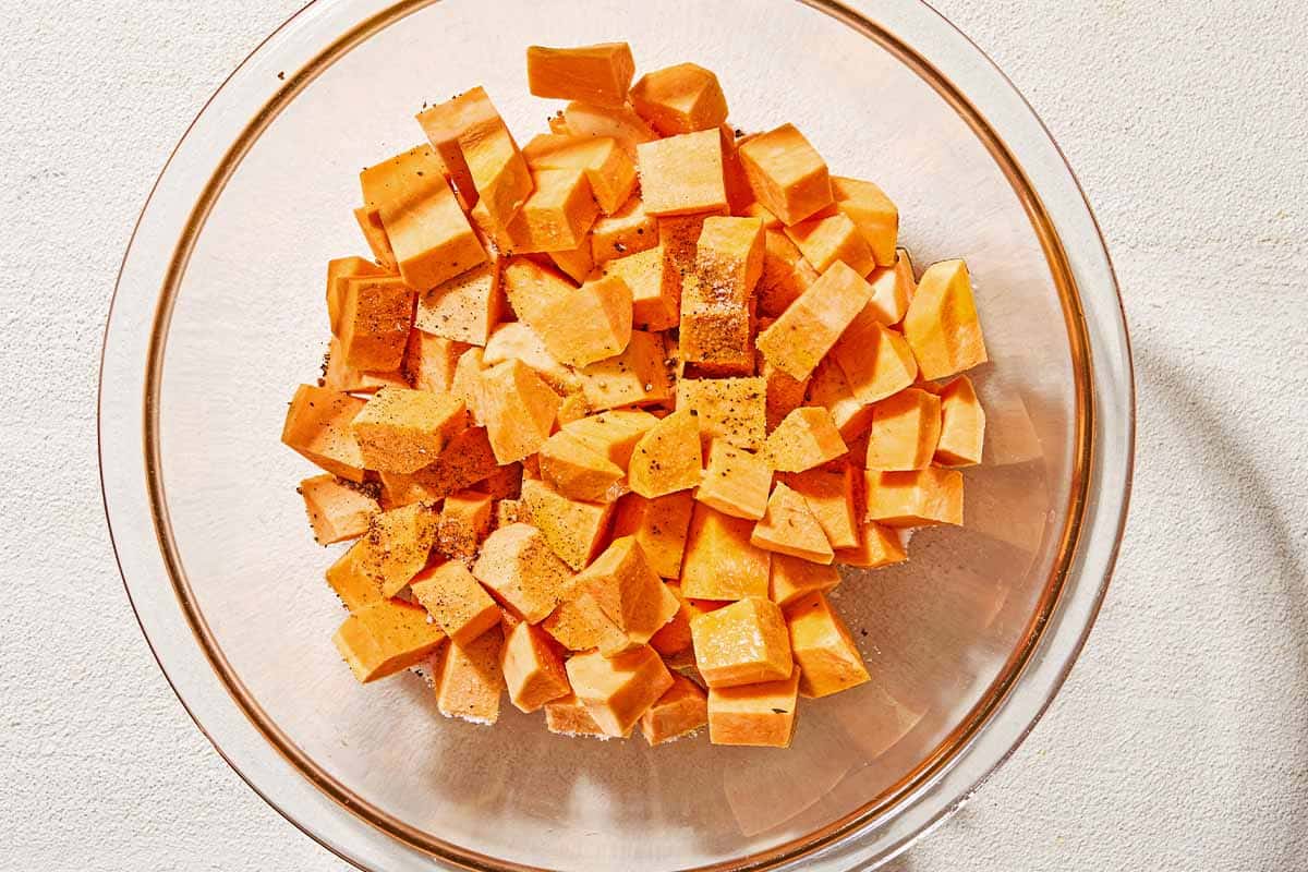 Seasoned cubes of uncooked sweet potato in a bowl.