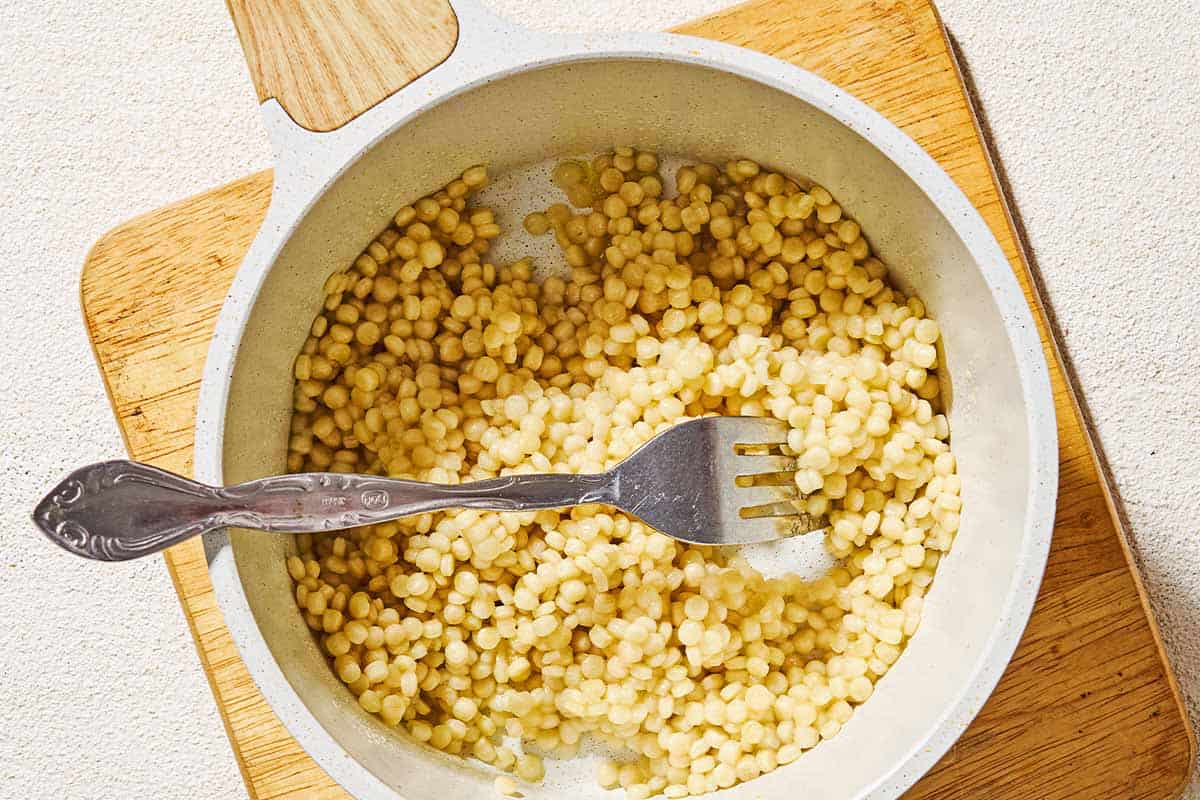 Cooked pearl couscous in a saucepan with a fork.