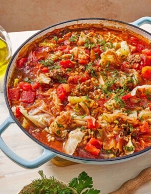 A close up of unstuffed cabbage rolls in a skillet. Next to this is a small bowl of Italian parsley and dill.