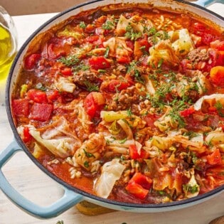 A close up of unstuffed cabbage rolls in a skillet. Next to this is a small bowl of Italian parsley and dill.