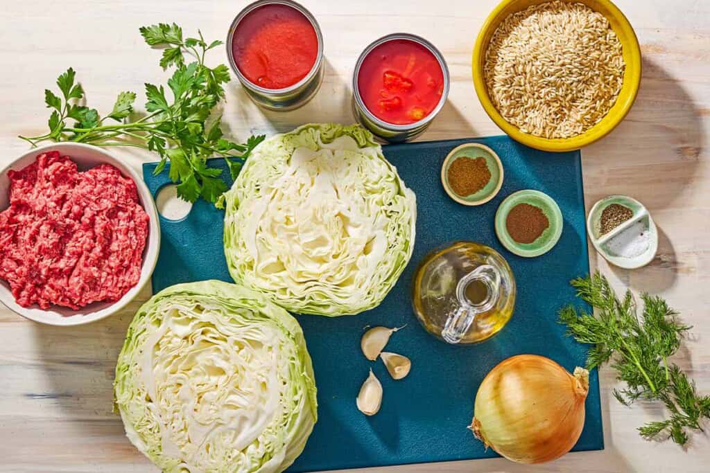 Ingredients for unstuffed cabbage rolls including green cabbage, ground beef, olive oil, onion, garlic, salt, black pepper, brown rice, italian parsley, dill, allspice, cumin, canned diced tomatoes and tomato sauce.