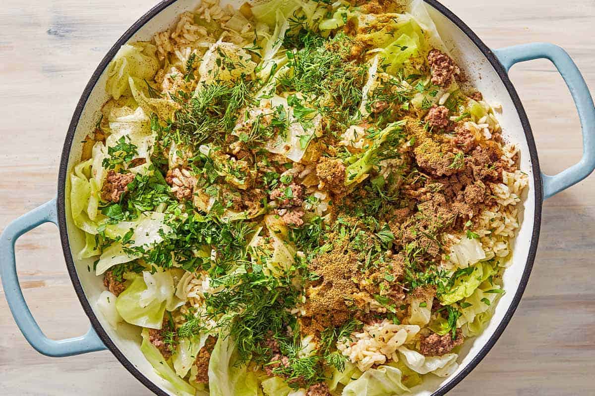 An overhead photo of the cooked cabbage, brown rice, chopped herbs and spices in the skillet.