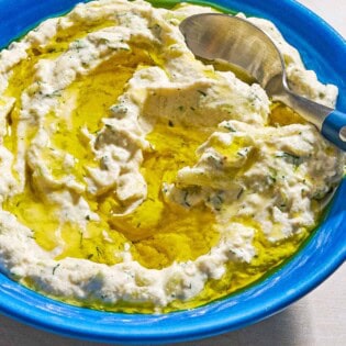 Vegan tzatziki sauce drizzled with olive oil in a bowl with a spoon.