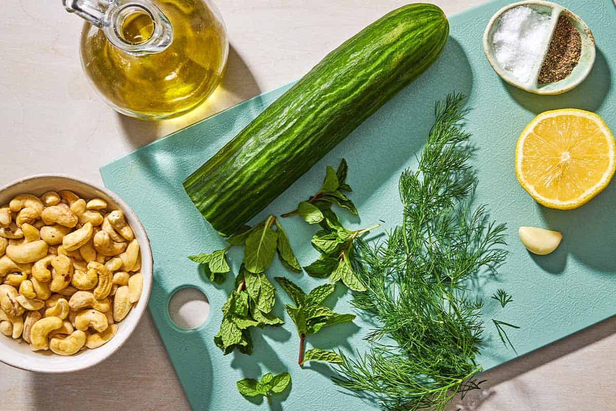 Ingredients for vegan tzatziki including cucumber, cashews, lemon, garlic, dill, mint, salt, pepper and olive oil.