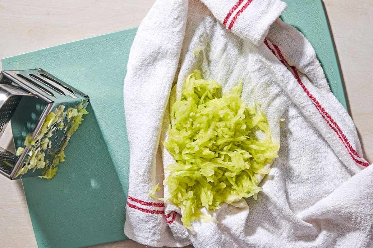 Shredded cucumber on a towel on a cutting board with a box grater.