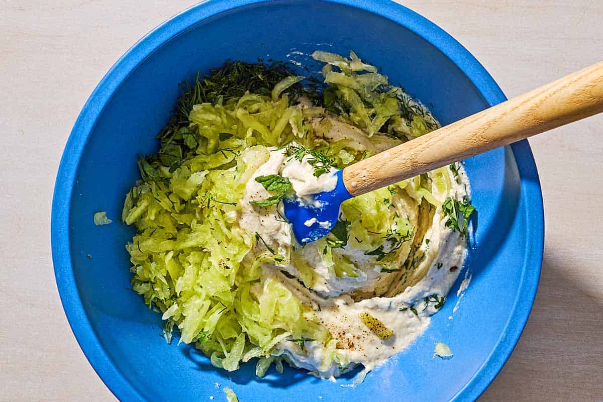 The ingredients for dairy free tzatziki in a bowl beginning to be stirred with a spatula.