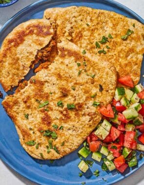 Stuffed flatbreads filled with harissa carrots and lentils on a plate with a cucumber tomato salad.