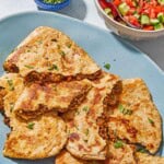 Stuffed pieces of whole wheat flatbread on a platter next to a tomato cucumber salad in a bowl with a spoon.