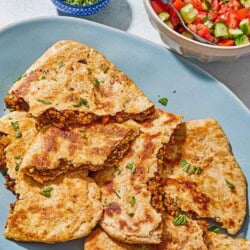 Stuffed pieces of whole wheat flatbread on a platter next to a tomato cucumber salad in a bowl with a spoon.