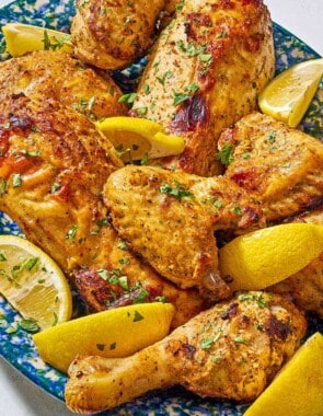 Pieces of cooked yogurt marinated chicken on a platter with lemon wedges.