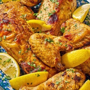 Pieces of cooked yogurt marinated chicken on a platter with lemon wedges.