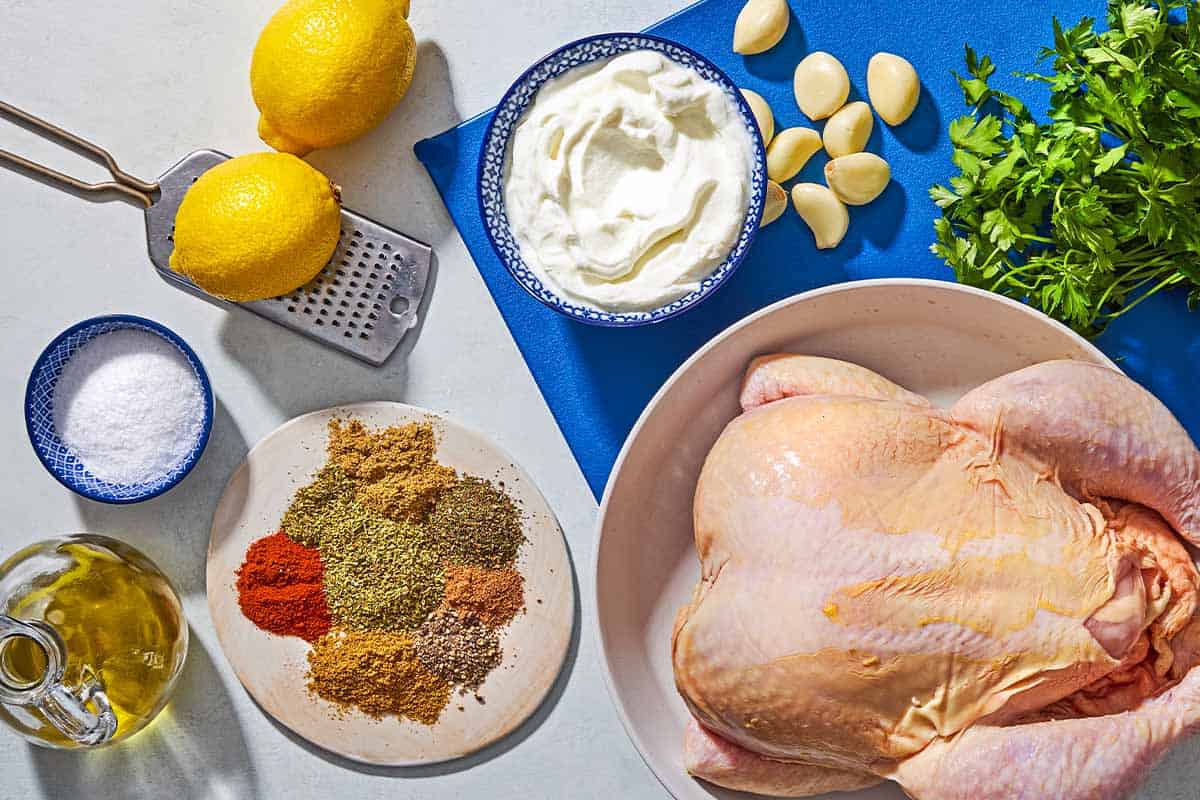 Ingredients for yogurt marinaded chicken including a whole chicken, garlic, parsley, yogurt, lemons, olive oil, oregano, mint, cumin, coriander, paprika, nutmeg, salt and black pepper.