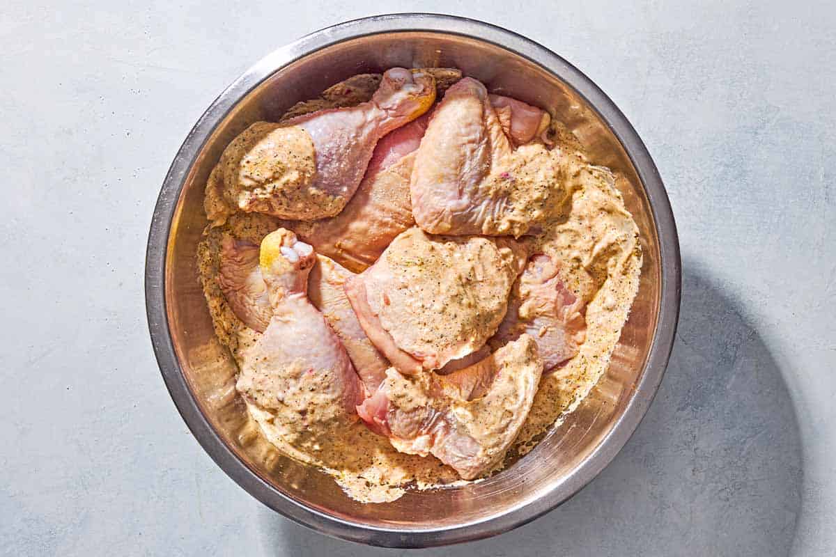 Pieces of uncooked chicken resting in the yogurt marinade in a mixing bowl.